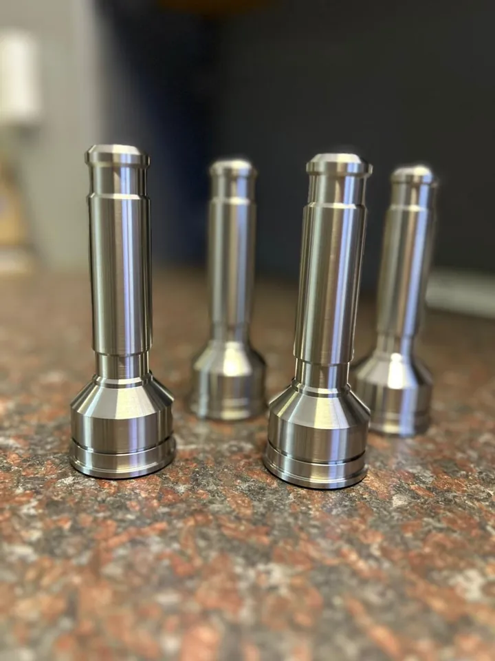 Four turned stainless steel filler nozzles standing in a row