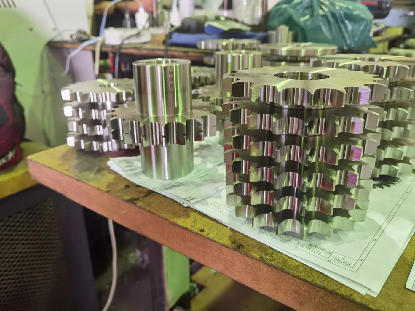 Batch of machined stainless steel sprockets and hubs stacked on their drawings